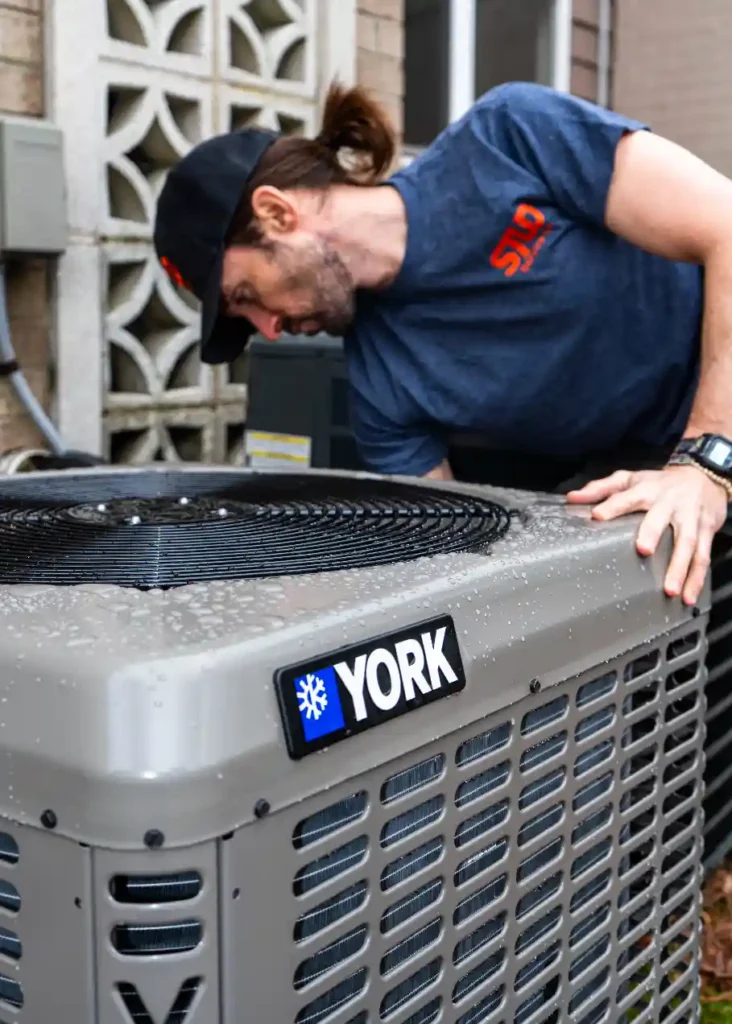 A person in a blue shirt inspects a York air conditioning unit outside a building.