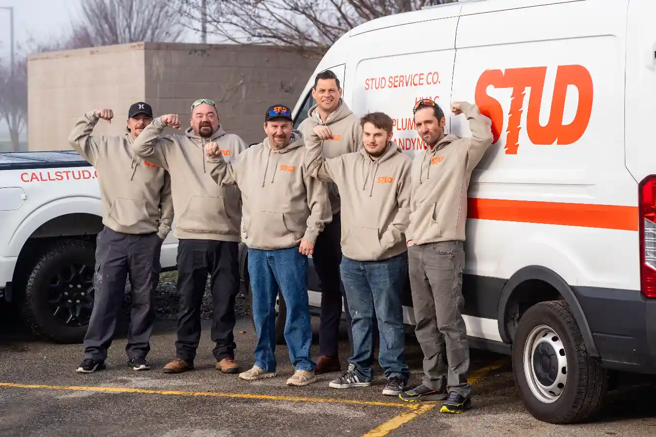 Six men in matching hoodies stand beside a white van labeled “STUD SERVICE CO.” in a parking lot, some with arms raised and flexed, posing for the photo.