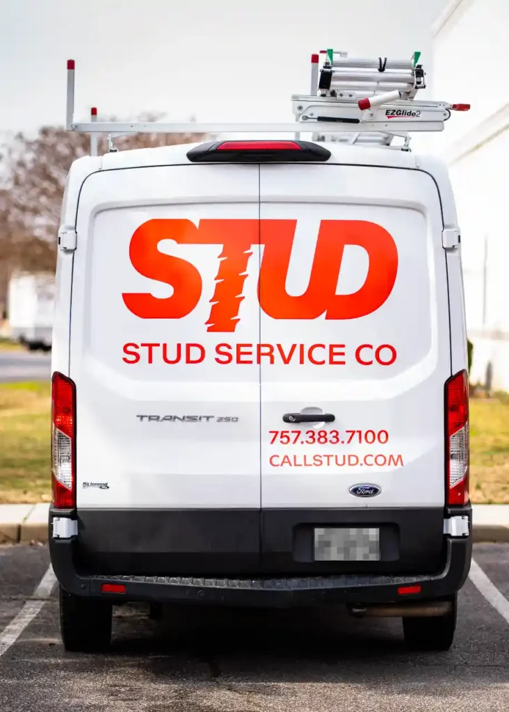 White van with “STUD SERVICE CO” and contact information in bold red letters on the back doors, parked in a lot. Ladder mounted on the roof.
